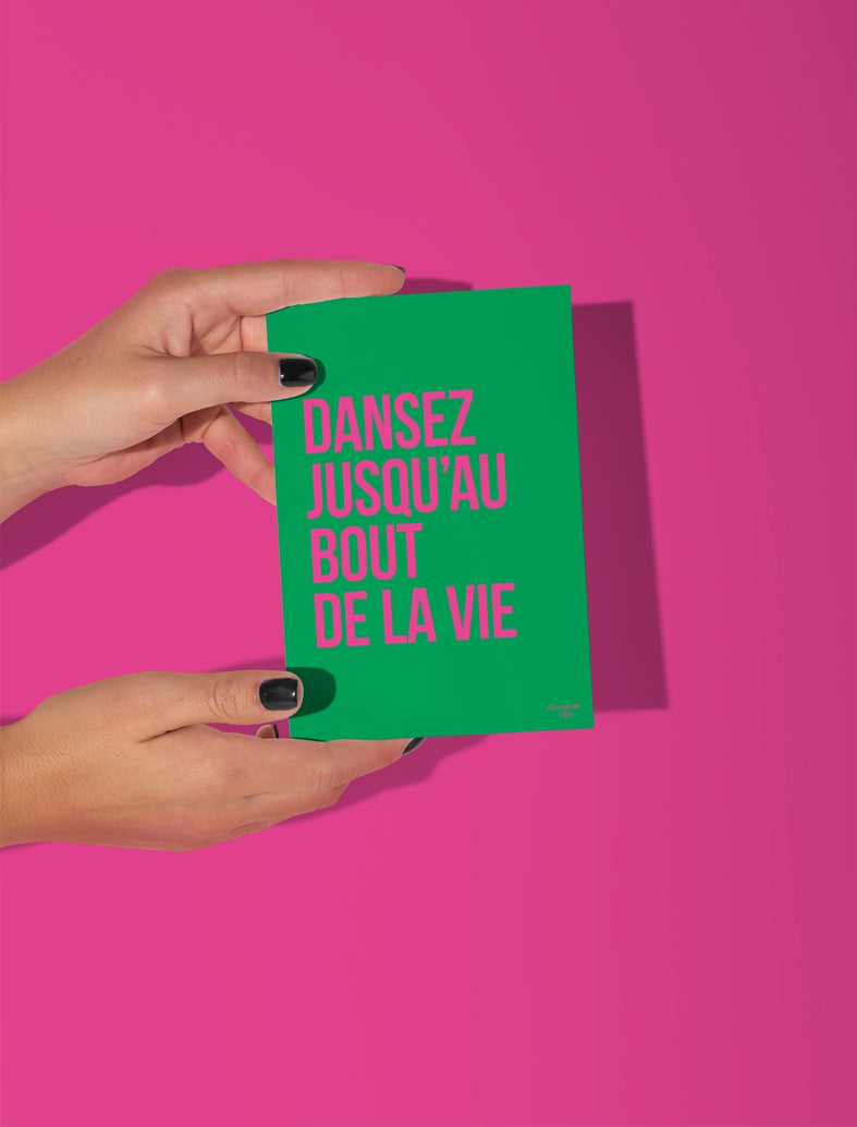 Carte postale écrit "dansez jusqu'au bout de la vie" en rose sur fond vert tenue par deux mains