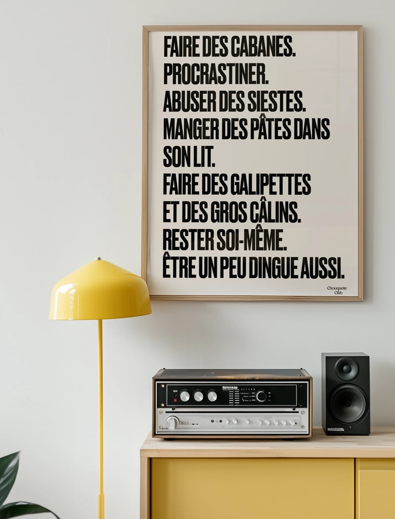 poster avec un mantra écrit dessus en noir et blanc dans un cadre en bois, dans un salon avec une lampe jaune et meuble jaune aussi