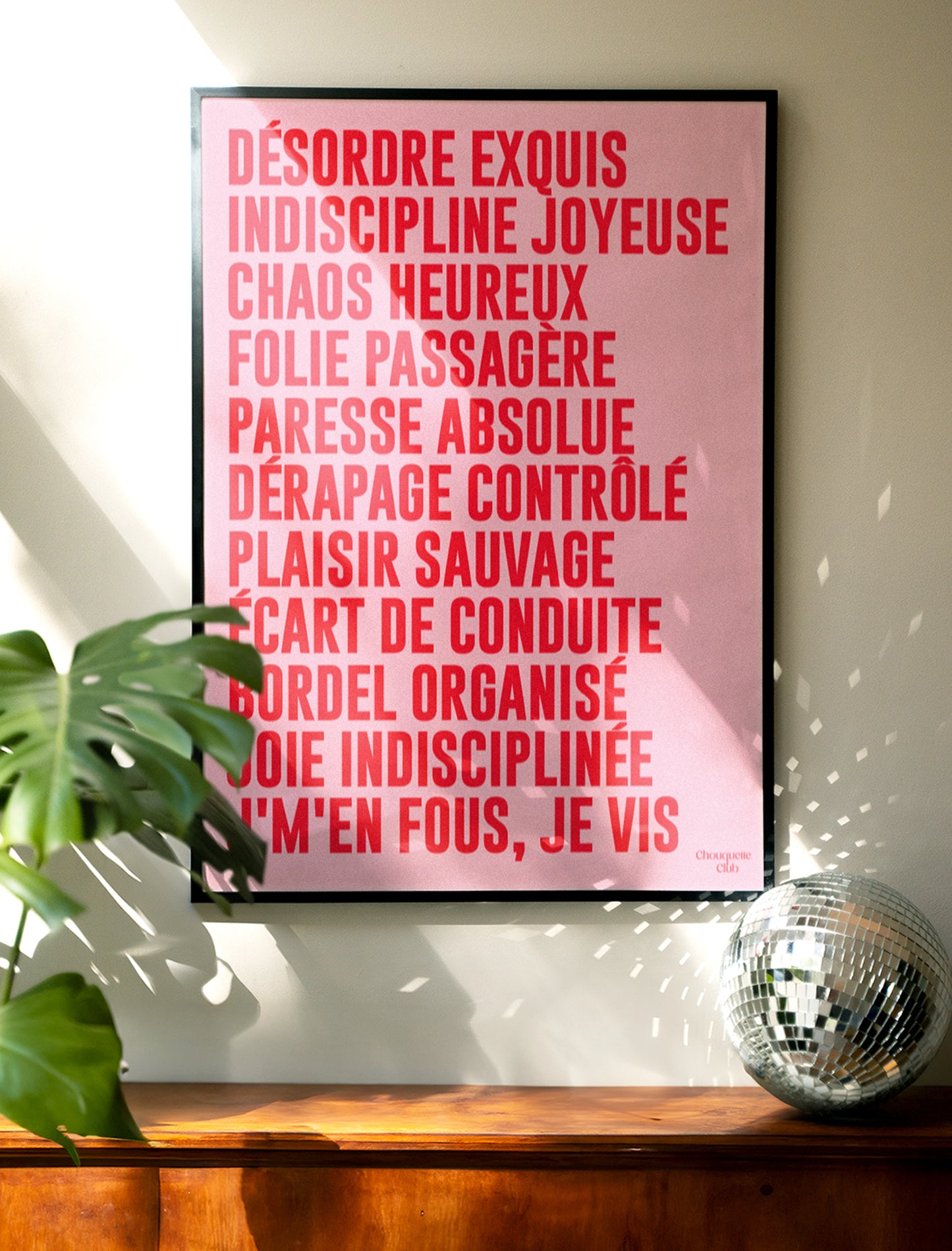 poster mantra rose et rouge de chouquette club accroché au mur dans un cadre noir et une boule à facettes posée sur le meuble