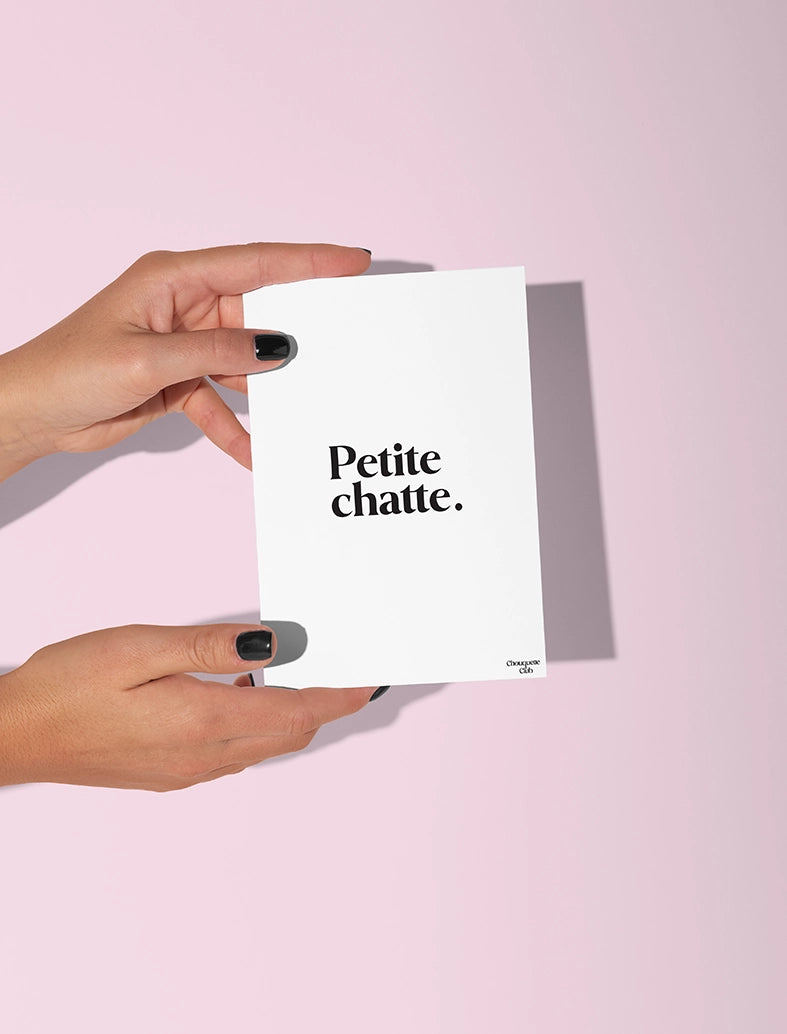 Deux mains qui tiennent une carte postale blanche avec écriture en noir dessus “ Petite chatte”