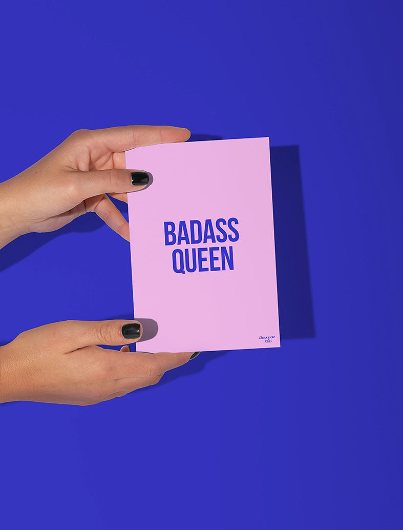 Carte postale rose tenue par deux mains, avec le texte bleu"Badass queen"