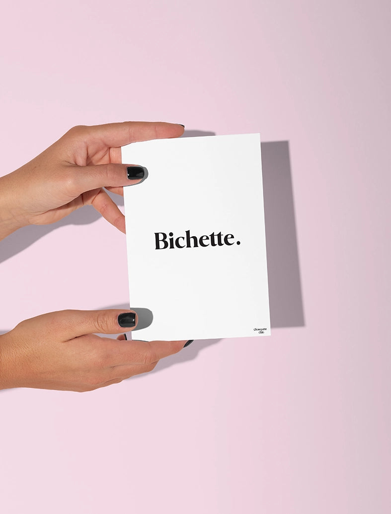 Deux mains qui tiennent une carte postale blanche avec écriture en noir dessus “ Bichette”