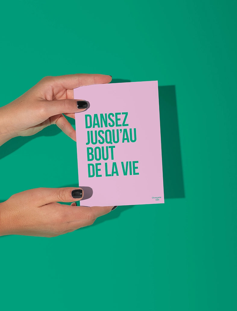 Carte postale rose tenue par deux mains, avec le texte "Dansez jusqu'au bout de la vie" en vert