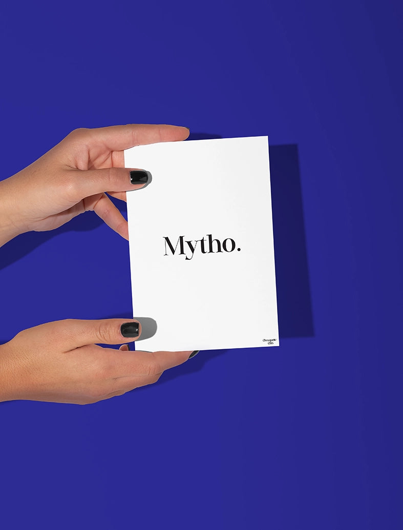 Deux mains qui tiennent une carte postale blanche avec écriture en noir dessus “Mytho”