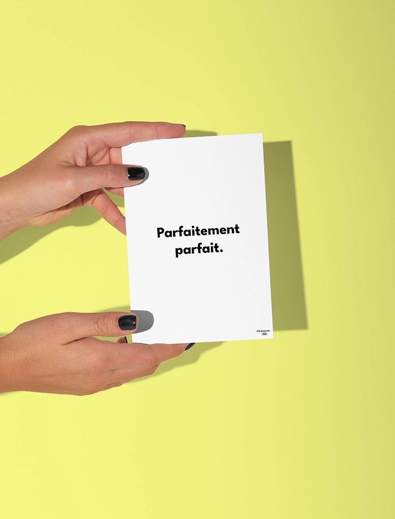 Deux mains qui tiennent une carte postale blanche avec écriture en noir dessus “Parfaitement parfait ”