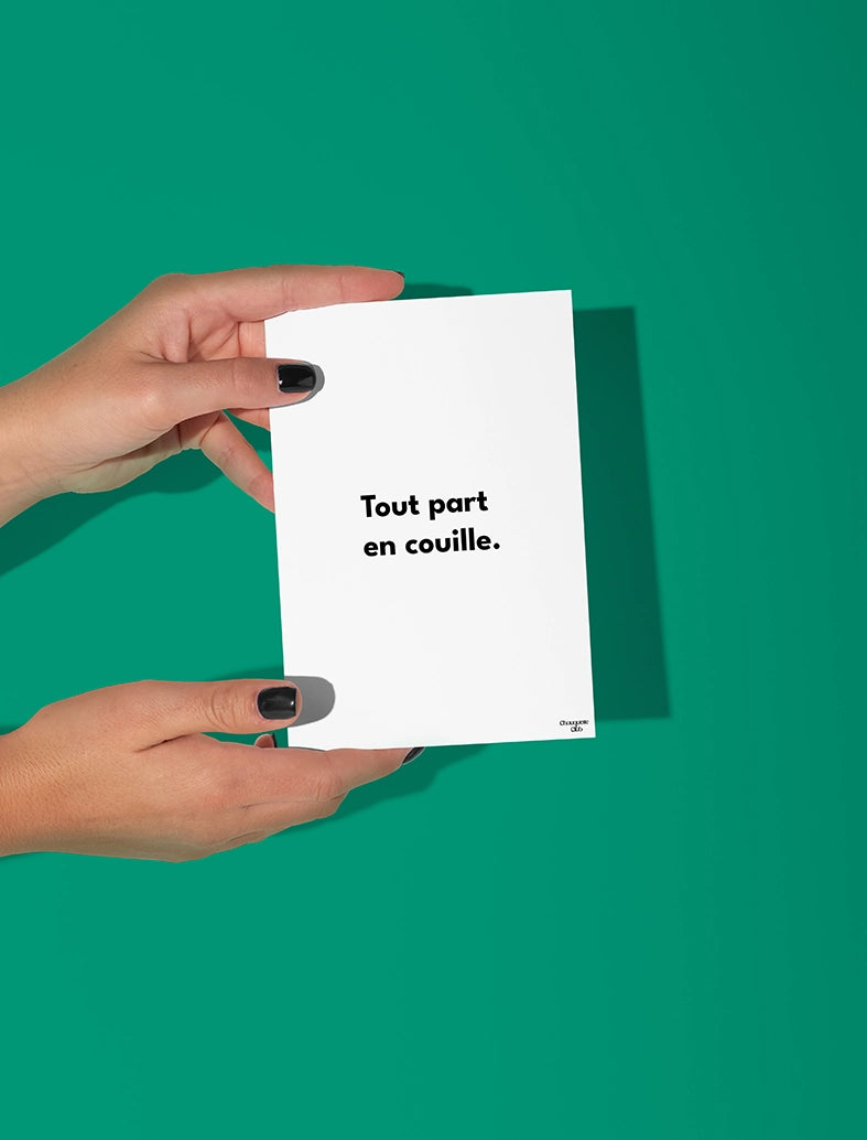 Deux mains qui tiennent une carte postale blanche avec écriture en noir dessus “Tout part en couille”.
