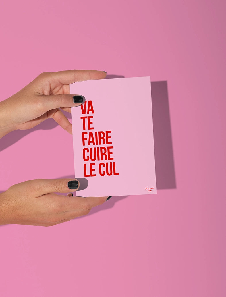 Deux mains qui tiennent une carte postale rose avec écrit dessus "Va te faire cuire le cul " en rouge