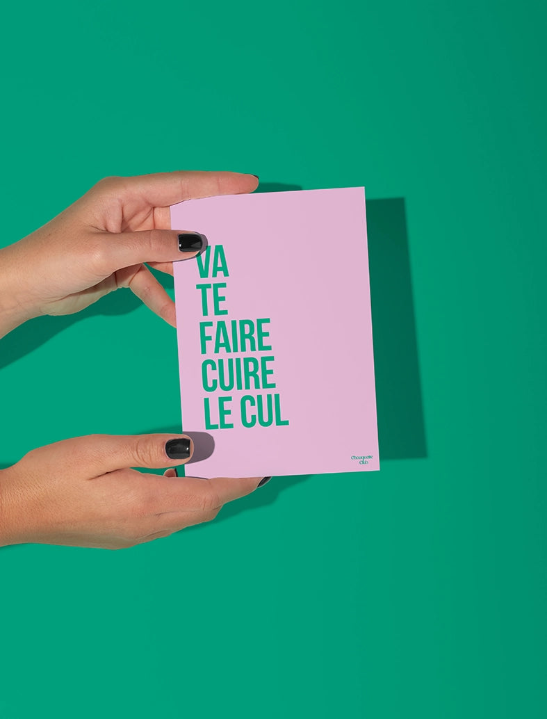 Mains qui tiennent une carte postale rose avec des écritures en vert avec "va te faire cuire le cul"