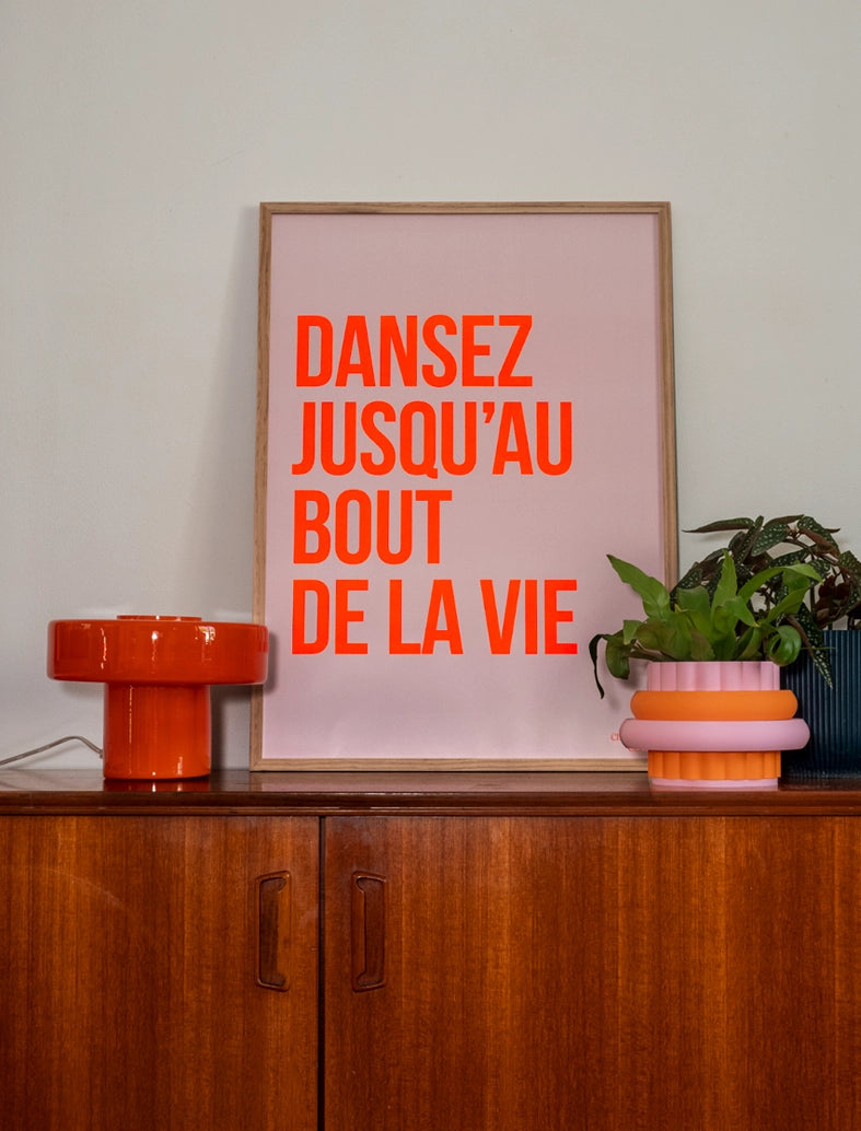 Poster "Dansez jusqu’au bout de la vie" avec Orange fluo dans un cadre en bois posé sur une enfilade vintage
