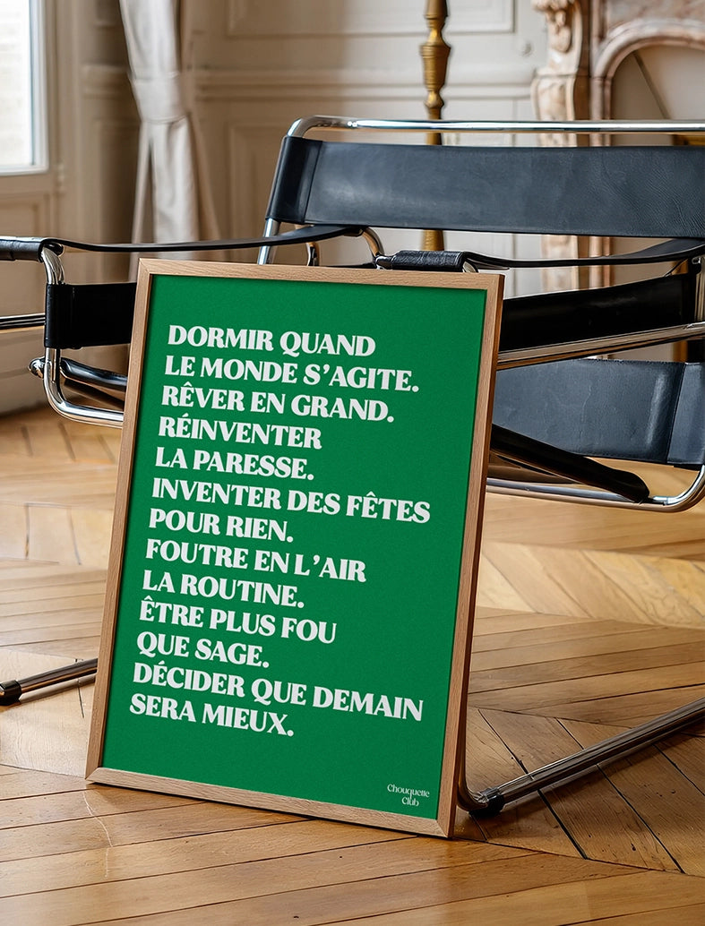 Mantra vert encadré au mur de la marque Chouquette Club posé au sol contre une chaise en cuir et acier dans un salon.