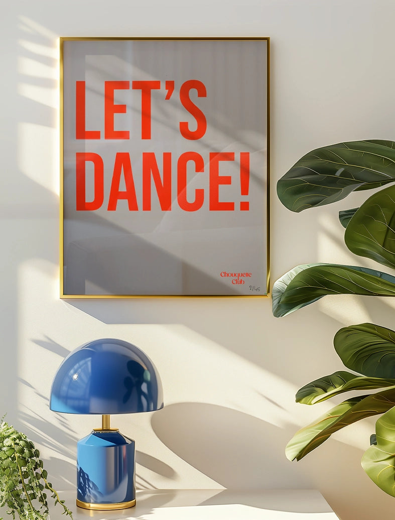 photo dans un salon avec une affiche sérigraphiée marquée let's dance en orange fluo sur un fond blanc dans un cadre doré
