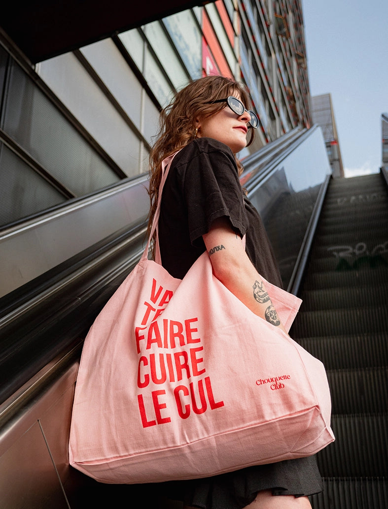 sac en coton rose et rouge de chouquette club marqué dessus "va te faire cuire le cul" porté par une jeune fille brune
