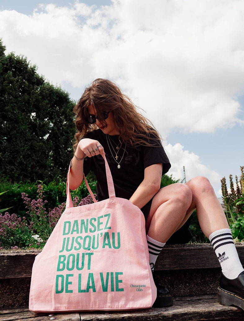 sac en coton rose et vert de chouquette club marqué dessus "dansez jusqu'au bout de la vie" avec une jeune fille aux cheveux longs et ondulés bruns
