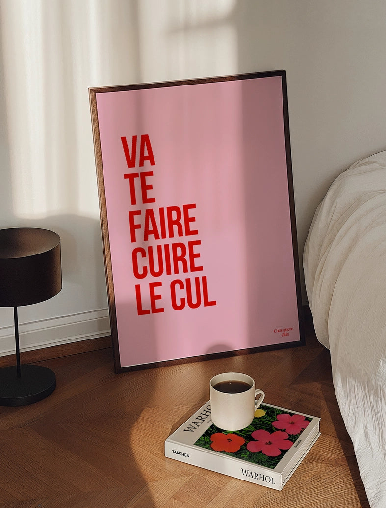 cadre avec affiche Va te faire cuire le cul rose et rouge posé sur un parquet dans une chambre