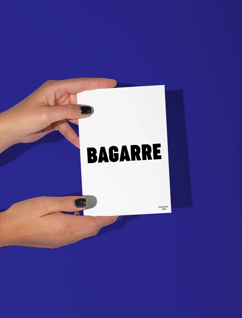 Deux mains qui tiennent une carte postale blanche avec écriture en noir dessus “bagarre".