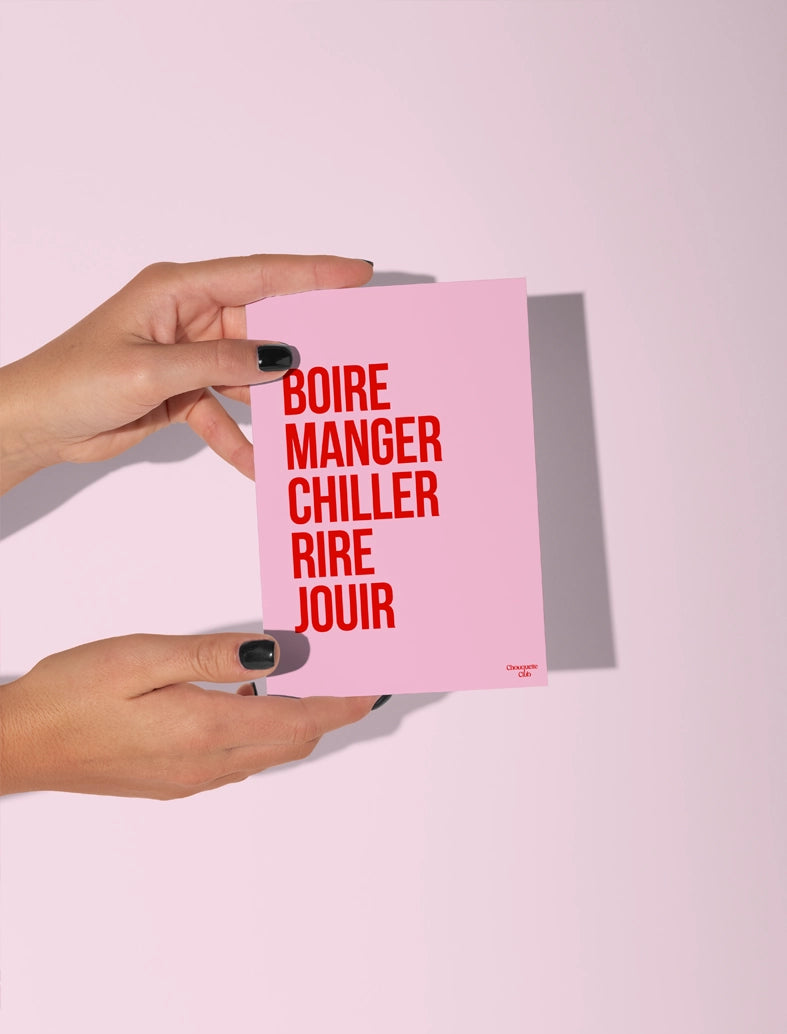 Carte postale rose tenue par deux mains, avec le texte rouge 'Boire manger chiller rire jouir