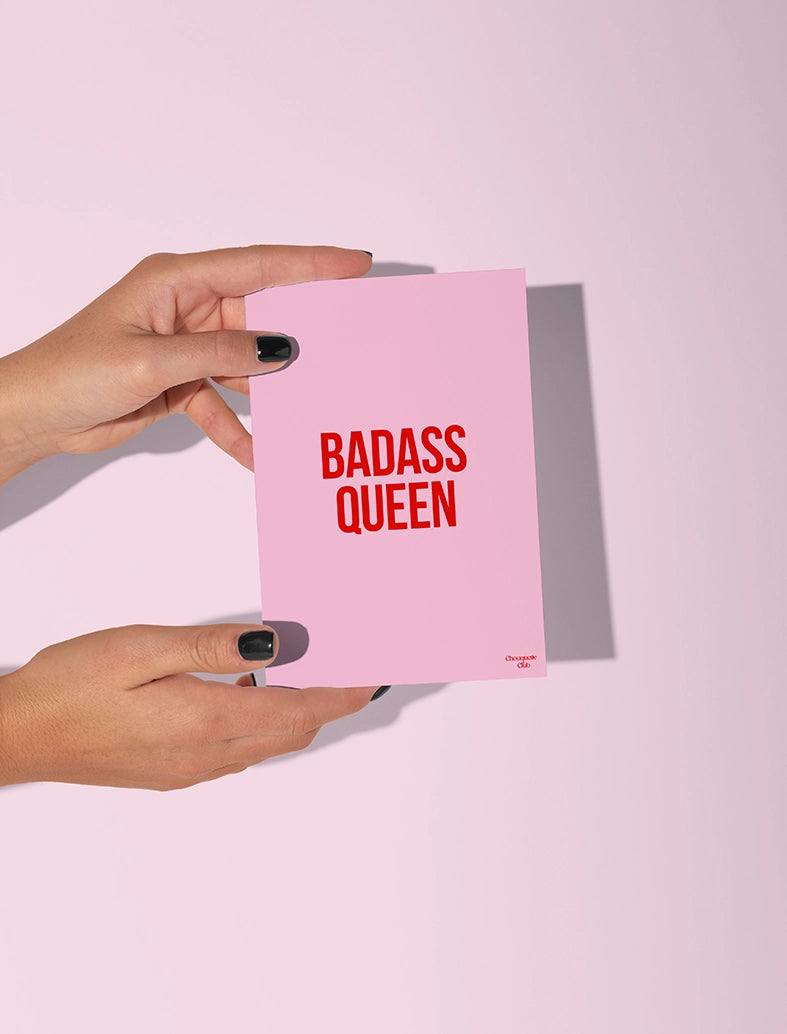 Carte postale rose tenue par deux mains, avec le texte en rouge "Badass queen"