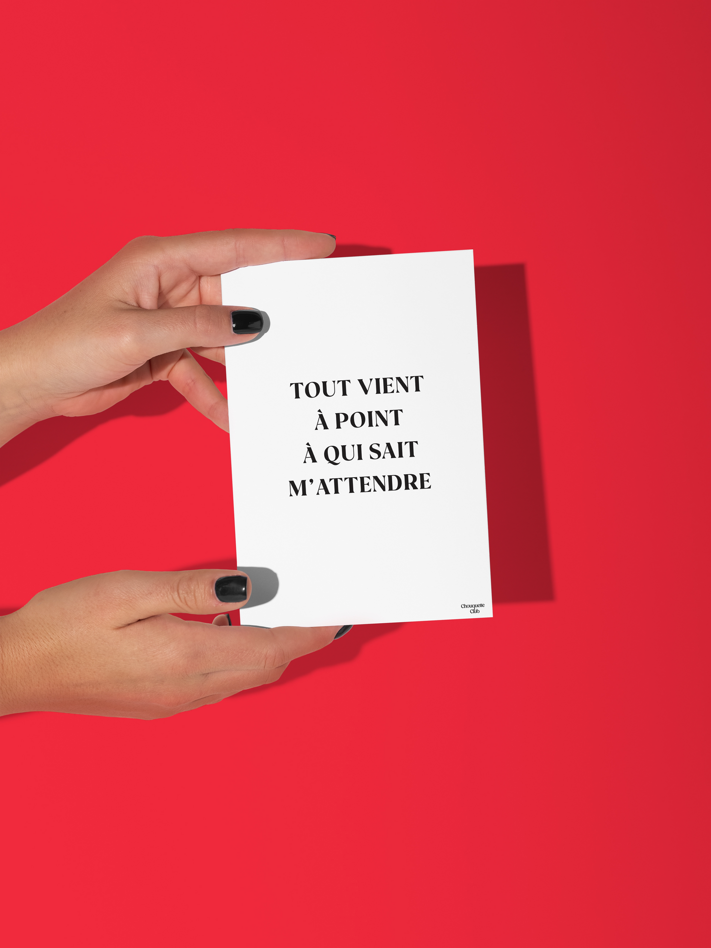 Deux mains qui tiennent une carte postale blanche écrit en noir "Tout vient à point à qui sait m'attendre"