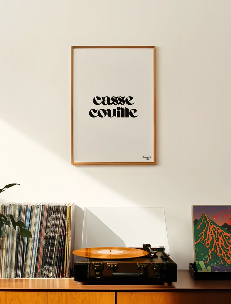 salon avec une affiche accrochée au mur dans un cadre en bois avec une affiche Casse-couille affiche en noir et blanc