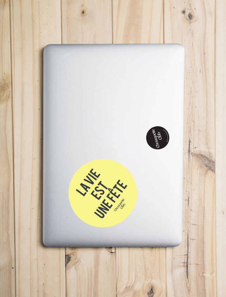Sticker « La vie est une fête » jaune et gris foncé collé sur un ordinateur