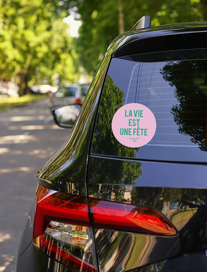 Sticker « La vie est une fête » rose et vert collé sur une voiture