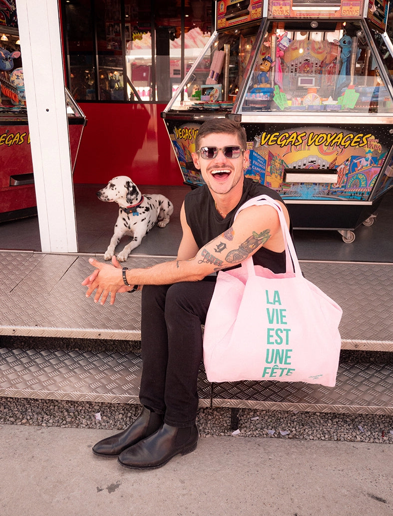 sac en coton rose et vert de chouquette club marqué dessus "la vie est une fête" porté par une homme dans une fête foraine