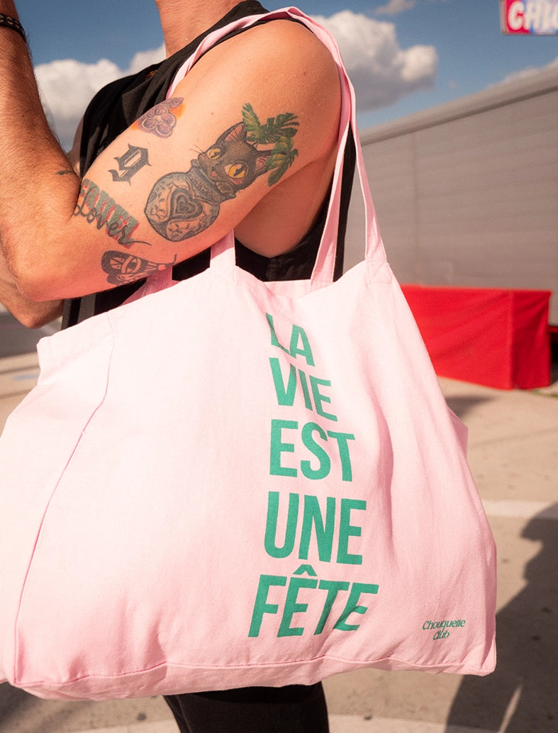 sac en coton rose et vert de chouquette club marqué dessus "la vie est une fête" porté par une homme dans une fête foraine