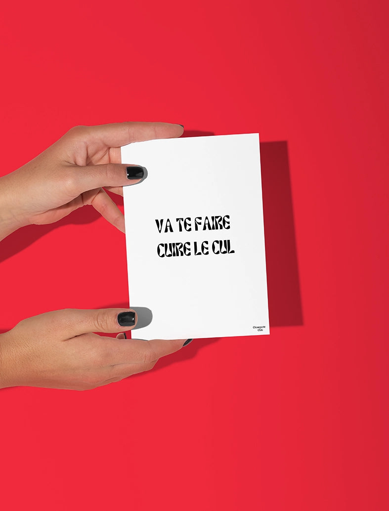 Deux mains qui tiennent une carte postale blanche avec écriture en noir dessus “Va te faire cuire le cul ”.