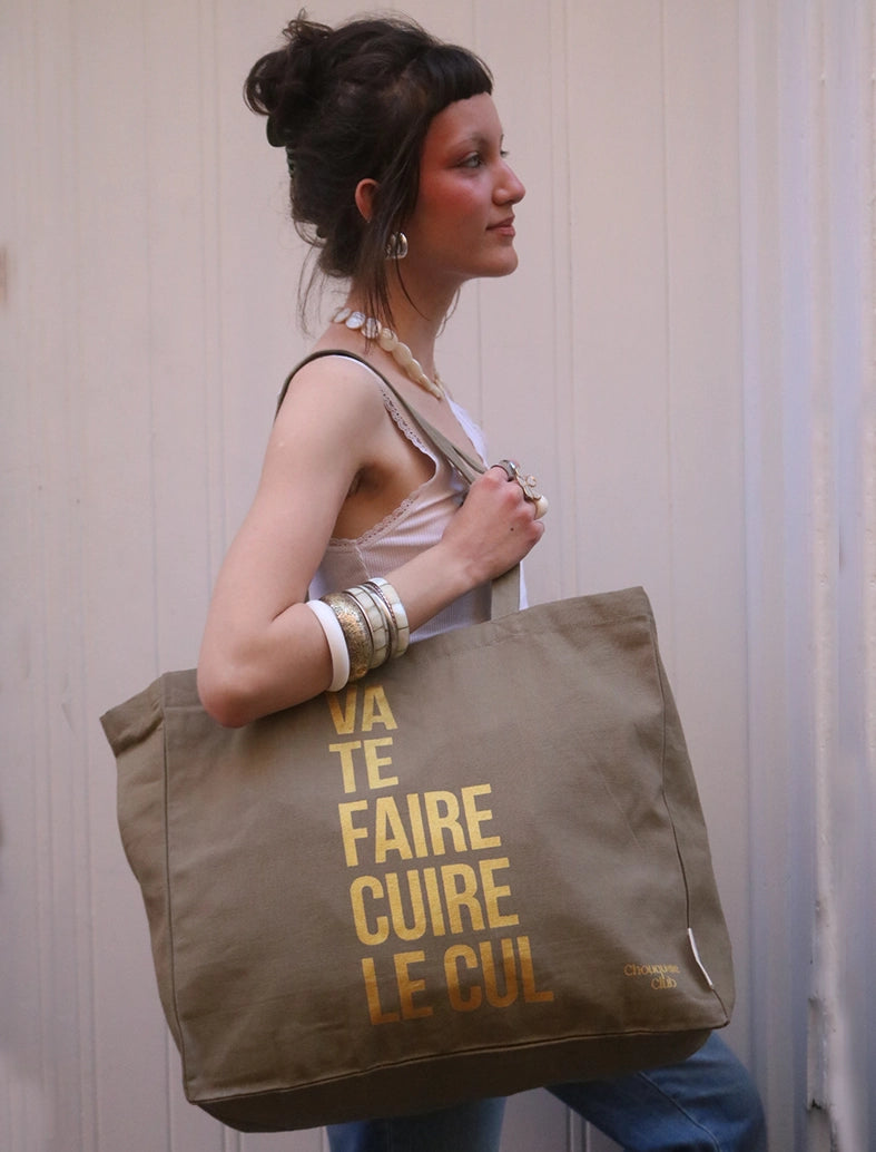 Tote bag XL en coton bio "Va te faire cuire le cul" kaki et doré porté par une jeune fille brune