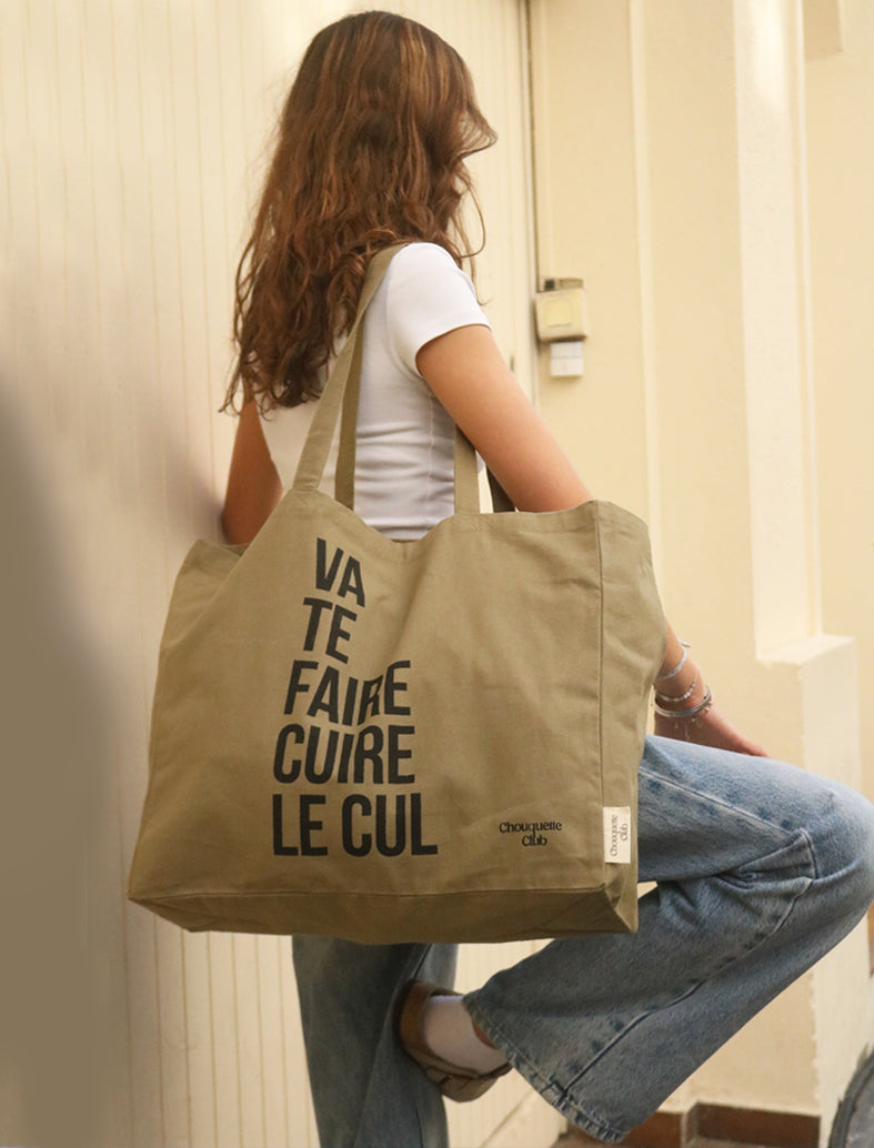 Tote bag XL en coton bio "Va te faire cuire le cul" kaki et noir porté par une jeune fille brune