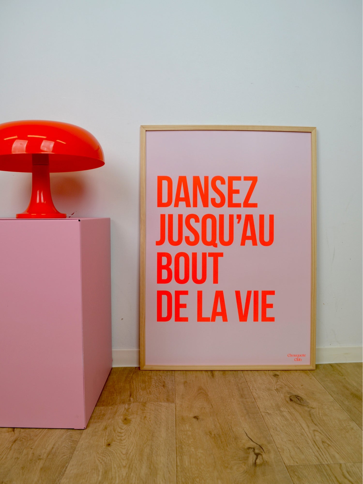 Poster "Dansez jusqu’au bout de la vie" avec  Orange fluo dans un cadre en bois posé au sol sur du parquet