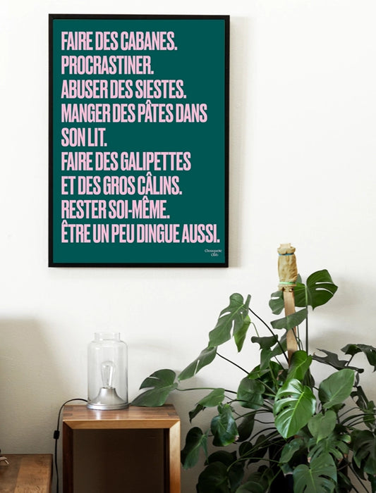 poster chouquette club vert sapin avec un mantra écrit dessus en rose dans un cadre en bois noir dans un chambre avec une plante 