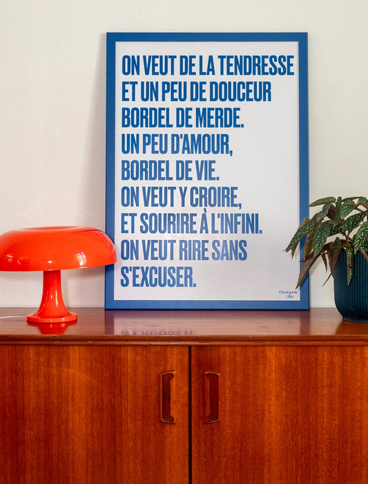poster avec un mantra écrit dessus en bleu dans un cadre en bois bleu, dans un salon avec une lampe orange