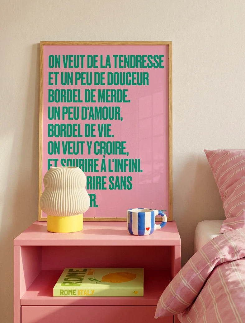 poster avec un mantra écrit dessus en rose et vert dans un cadre en bois, dans une chambre avec une lampe et une housse de couette rose