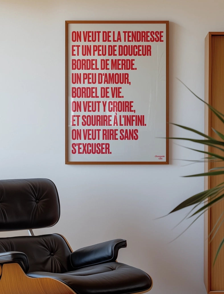 poster avec un mantra écrit dessus en rouge dans un cadre en bois, dans un salon avec fauteuil en cuir vintage