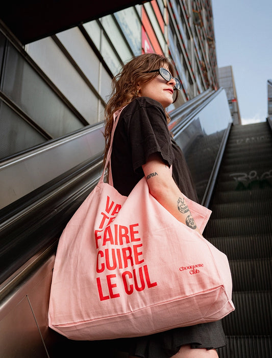 sac en coton rose et rouge de chouquette club marqué dessus "va te faire cuire le cul" porté par une jeune fille brune