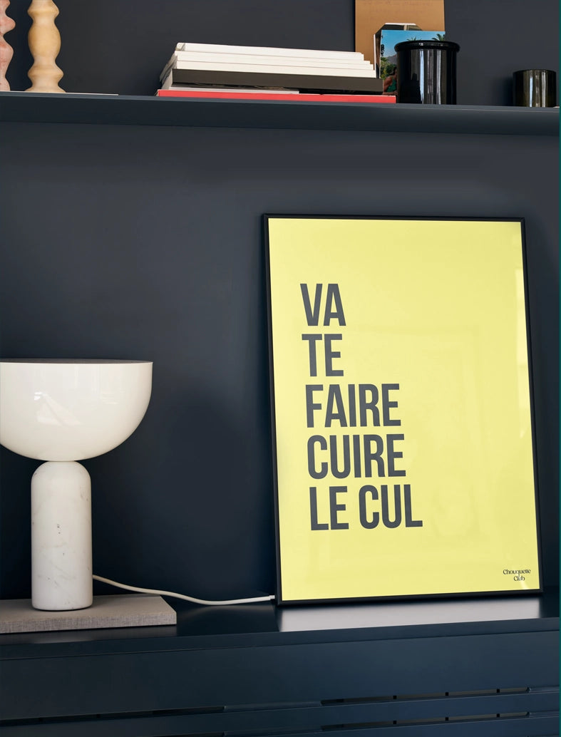 Va te faire cuire le cul affiche (jaune et noir) dans un cadre posé sur un rebord de meuble