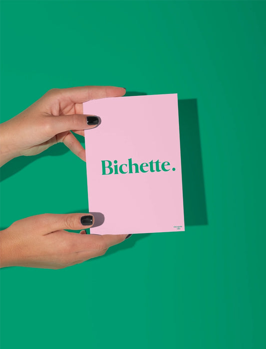 Deux mains qui tiennent une carte postale blanche avec écriture dessus “ Bichette” rose et vert
