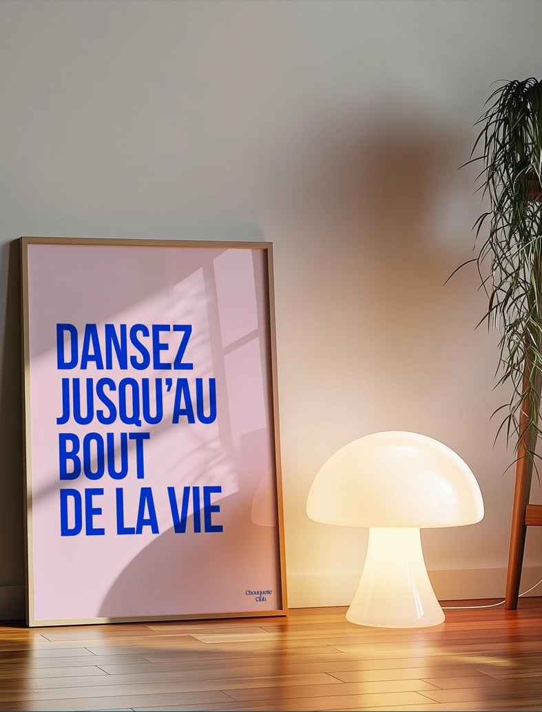 Dansez jusqu'au bout de la vie affiche (bleu électrique et rose pâle) de Chouquette Club posée au sol à côté d'une lampe