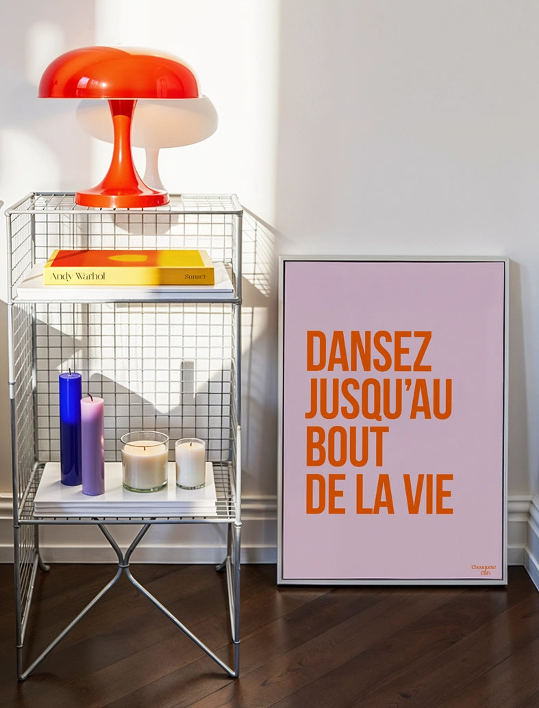 Dansez jusqu'au bout de la vie affiche (orange et rose pâle) posée sur un parquet au sol