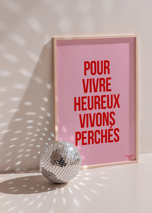 Affiche rose et rouge avec la phrase “Pour vivre heureux vivons perchés” – style typographique moderne Chouquette Club. dans un cadre à côté d'une boule à facettes