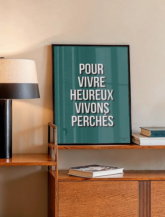Affiche vert sapin avec la phrase “Pour vivre heureux vivons perchés” – style typographique moderne Chouquette Club. dans un cadre dans un salon
