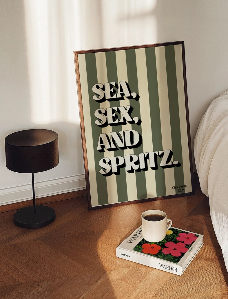 Affiche Sea, sex and spritz kaki et beige posée au sol dans une chambre