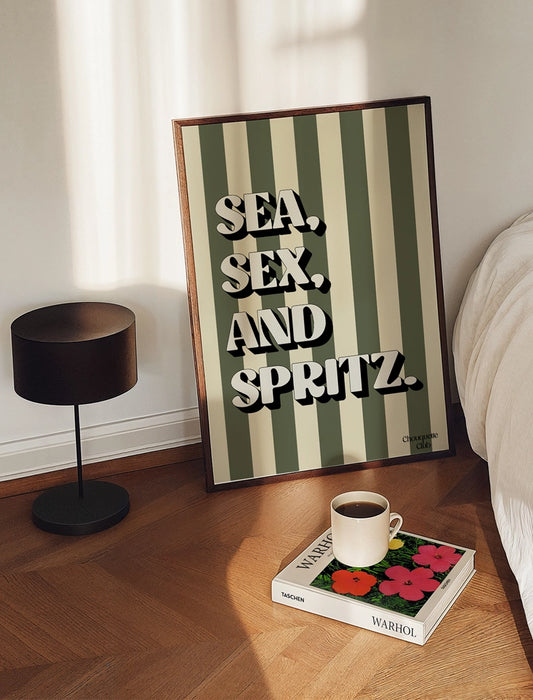 Affiche Sea, sex and spritz kaki et beige posée au sol dans une chambre