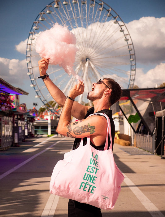 sac en coton rose et vert de chouquette club marqué dessus "la vie est une fête" porté par une homme dans une fête foraine