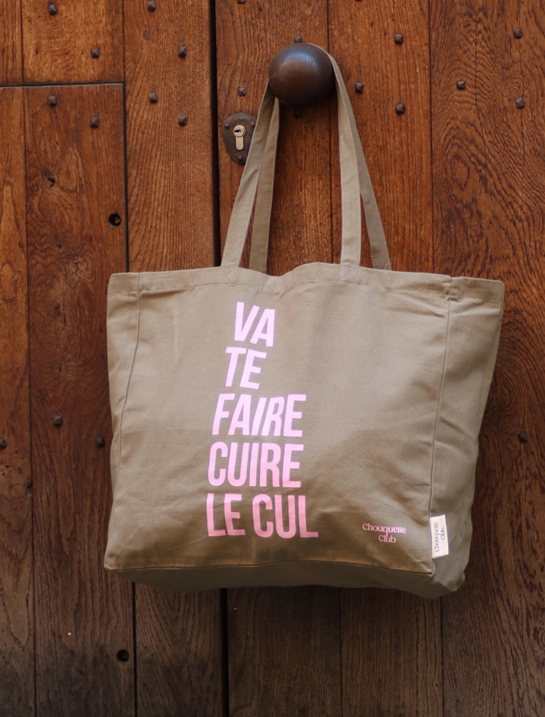 sac en coton kaki et rose de chouquette club marqué dessus "va te faire cuire le cul" accroché à une porte en bois