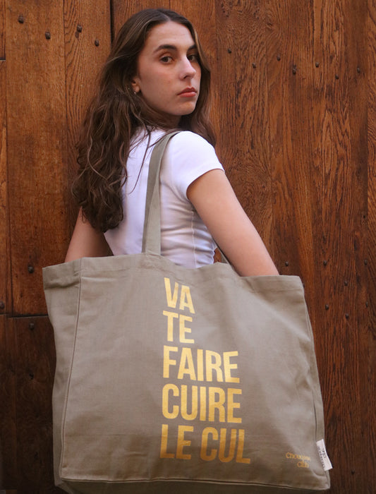 Tote bag XL en coton bio "Va te faire cuire le cul" kaki et doré porté par une jeune fille brune
