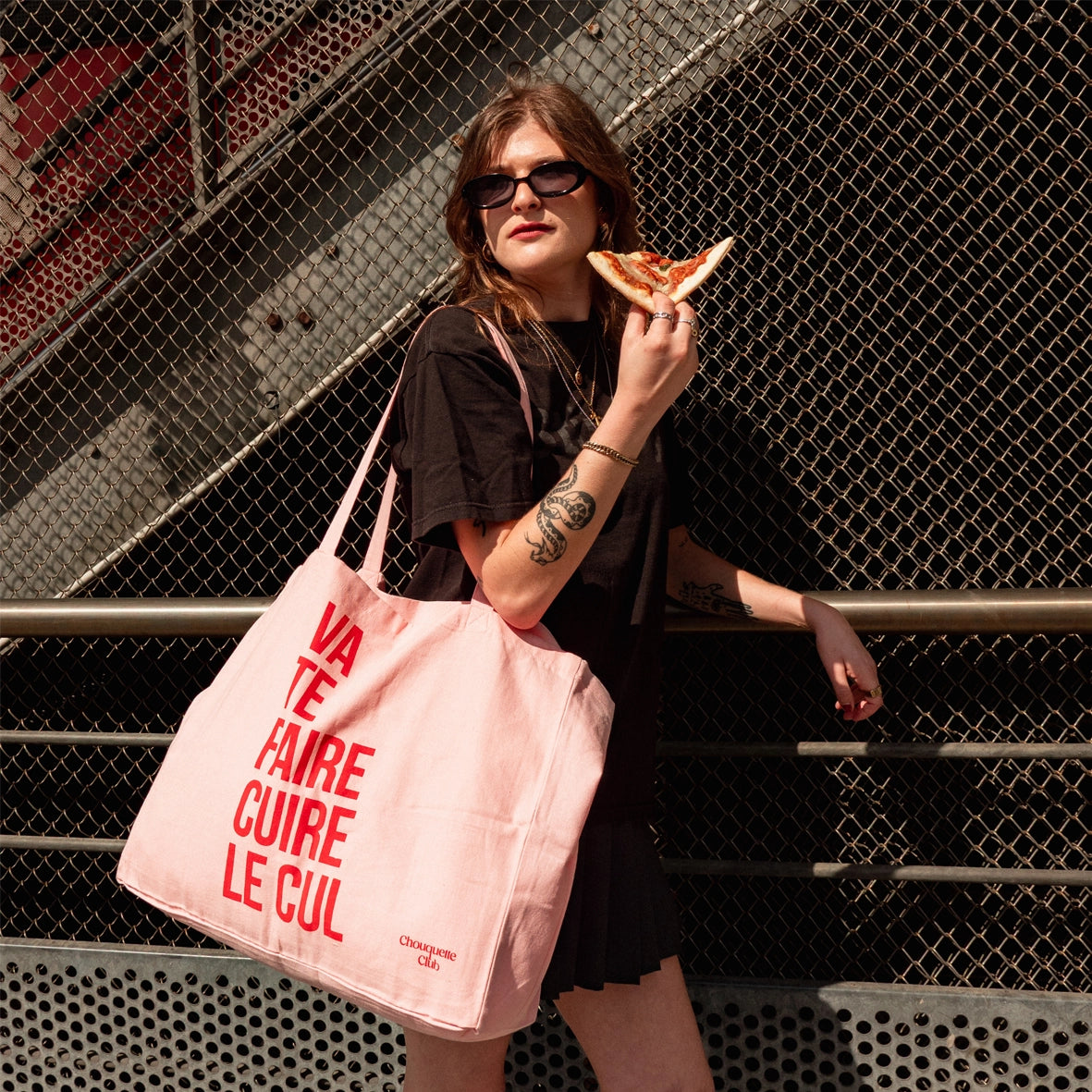 sac en coton rose et rouge de chouquette club marqué dessus "va te faire cuire le cul" porté par une fille brune aux longs cheveux