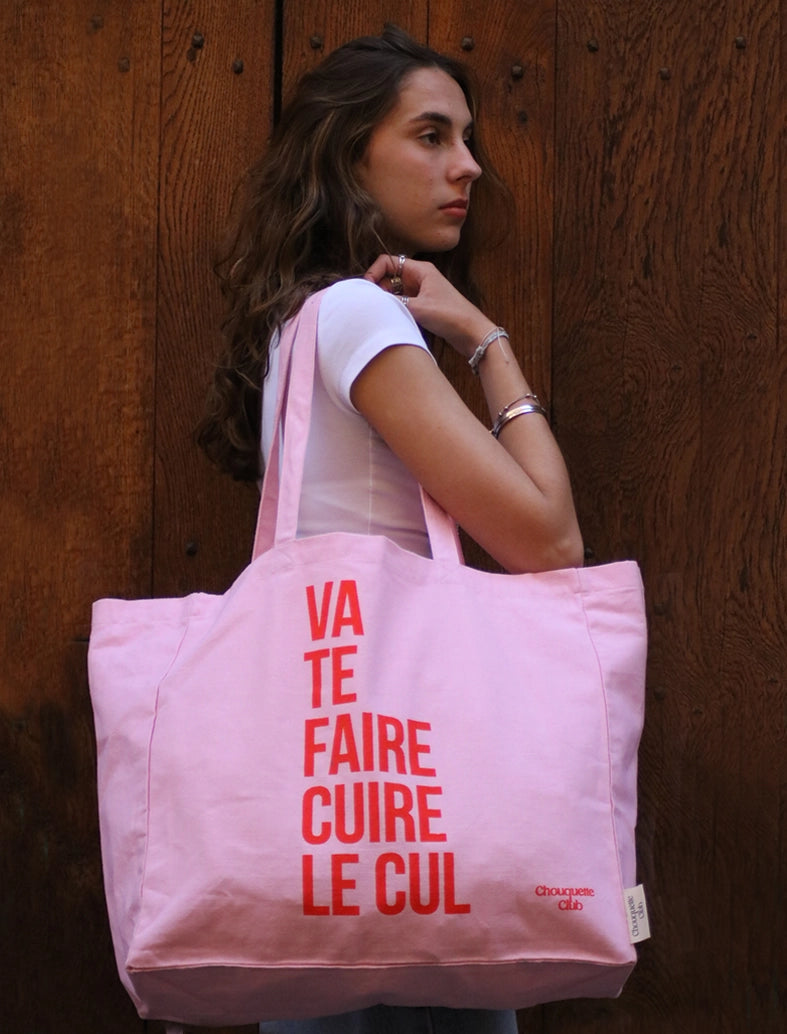 sac en coton rose et rouge de chouquette club marqué dessus "va te faire cuire le cul" porté par une fille brune aux longs cheveux